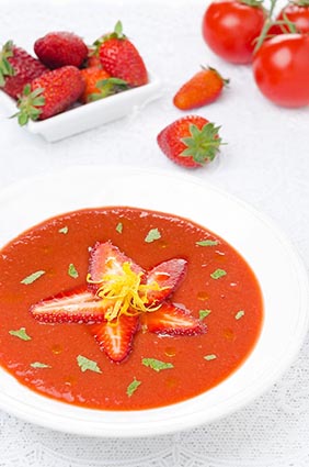 tomate y gazpacho de fresas en un plato, bayas frescas y tomates en el fondo, vertical